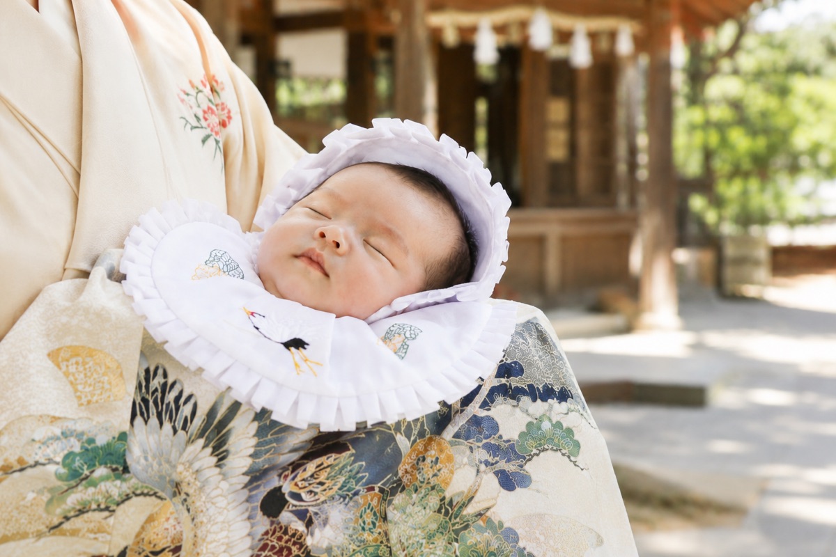 産着に包まれて眠る新生児。神社でのお宮参りの様子