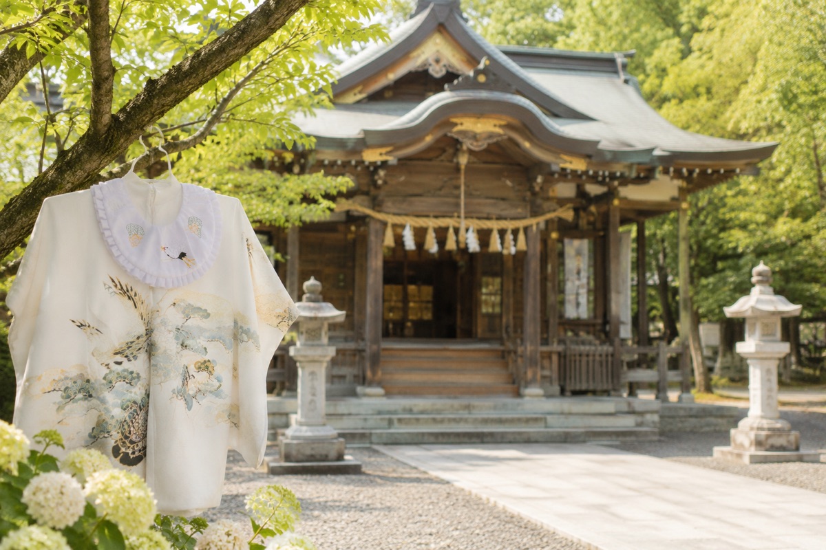 木に掛けられた産着と、緑に囲まれた神社。お宮参りの季節の情景