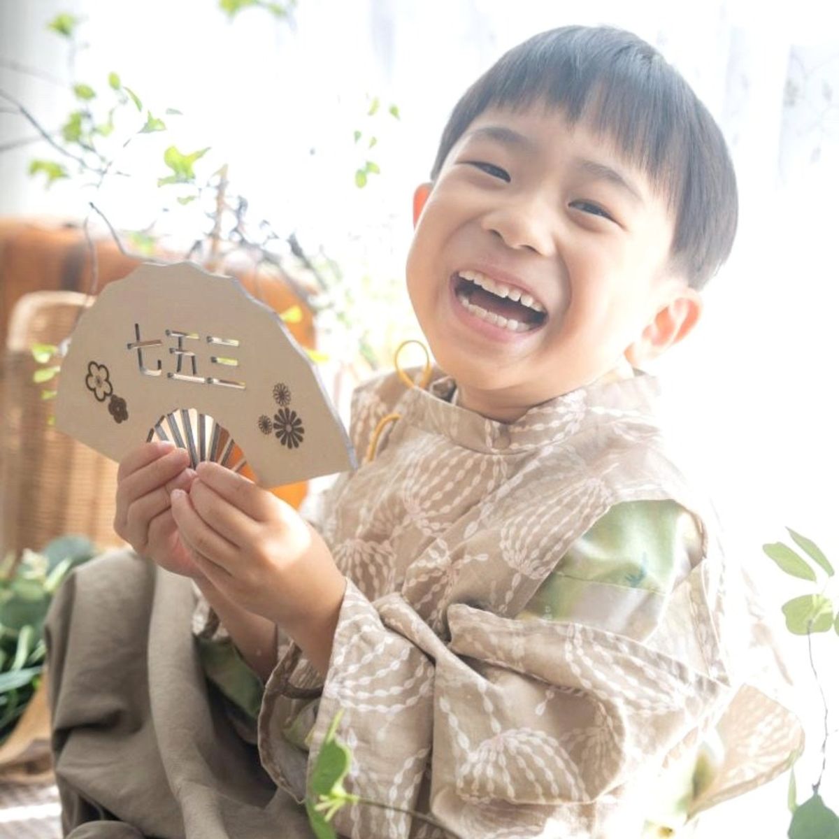 七五三の扇子プレートを持って笑う着物姿の男の子