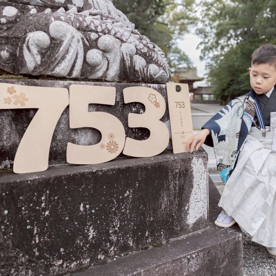 白い袴すがたの男の子が神社の狛犬の前で木製の753プレートを指さす様子
