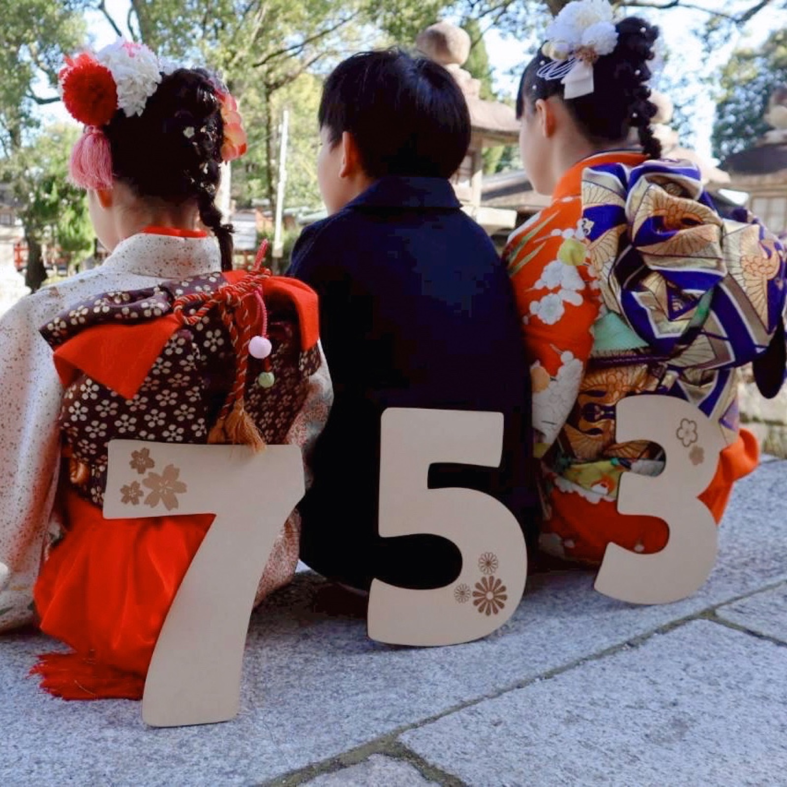 神社の石段に座る七五三の3人きょうだいと木製の753ビッグナンバー