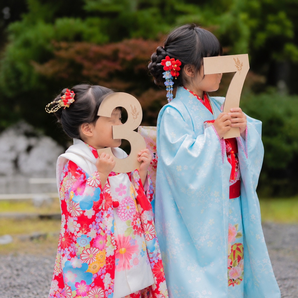 青い着物で結い上げの7歳女の子と妹が木製の753ナンバー小物を持つ様子