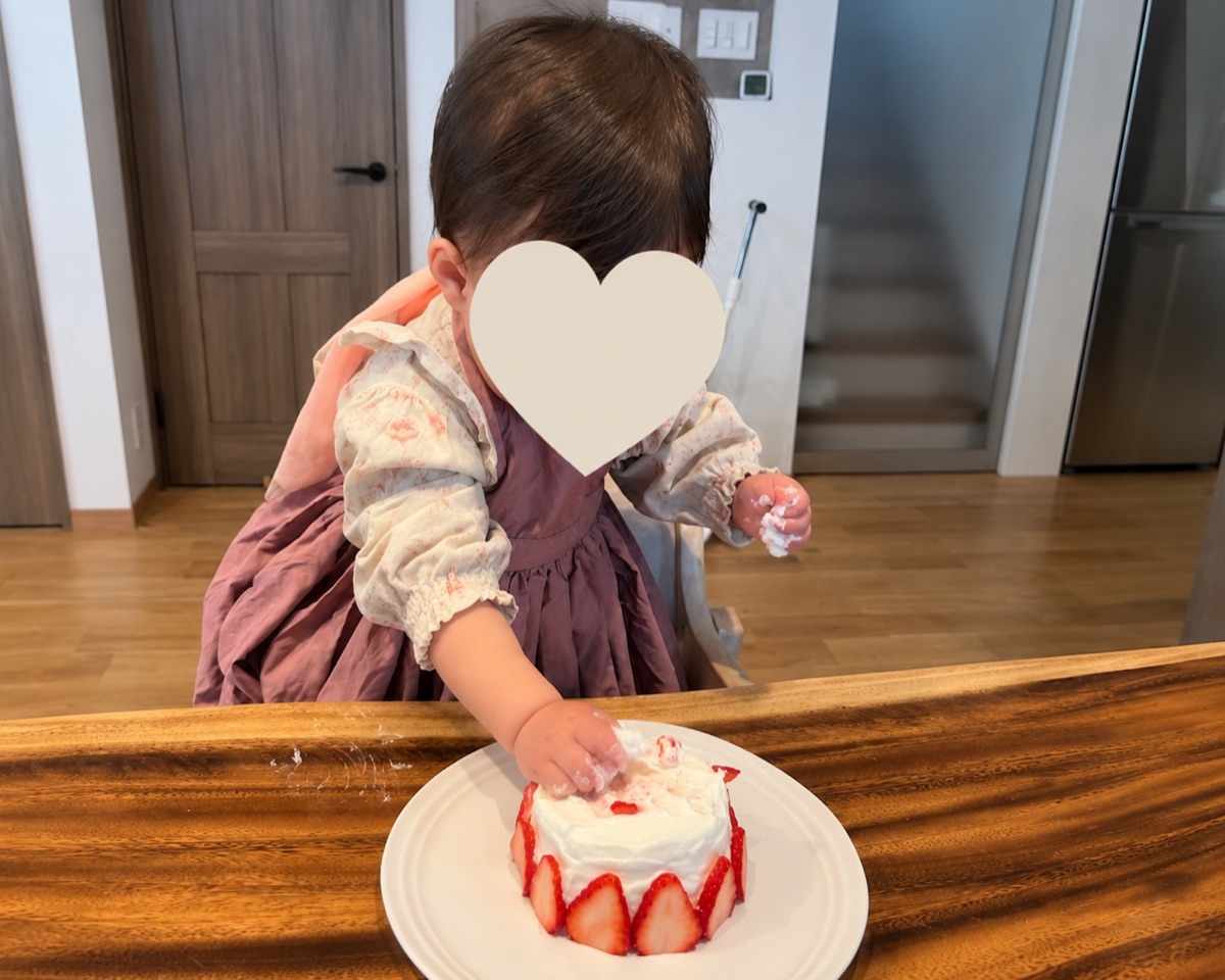 白いお皿のいちごスマッシュケーキにそっと手を伸ばす1歳の赤ちゃん